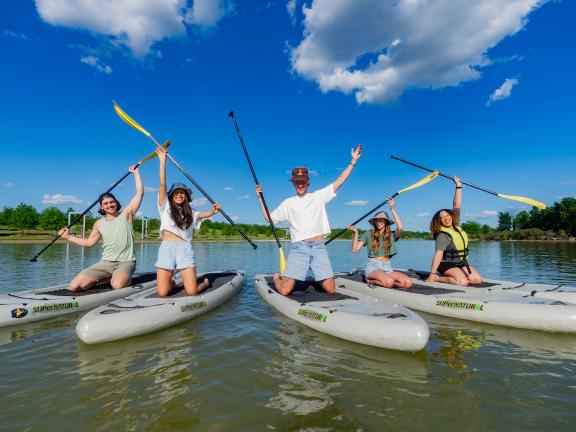 Group of paddle boarders pose for photo holding up oars on boards at Shelby Farms Park.