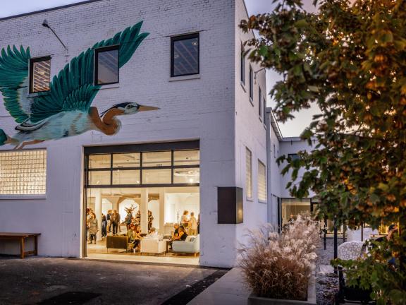 People inside the gallery space at Ugly Art Co with a large blueish-green bird mural above the entrance.
