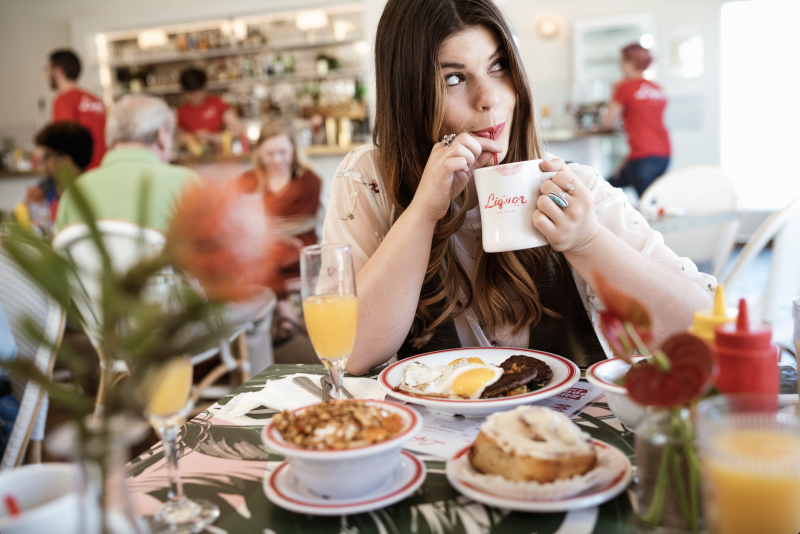 girl sips coffee with a table full of brunch food in front of her