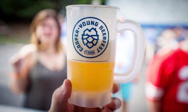 Plastic beer mug with handle and logo, half filled with beer, held up in front of out of focus crowd