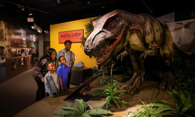 Family of four looking at a animatronic dinosaur at the Pink Palace Museum &amp; Mansion.