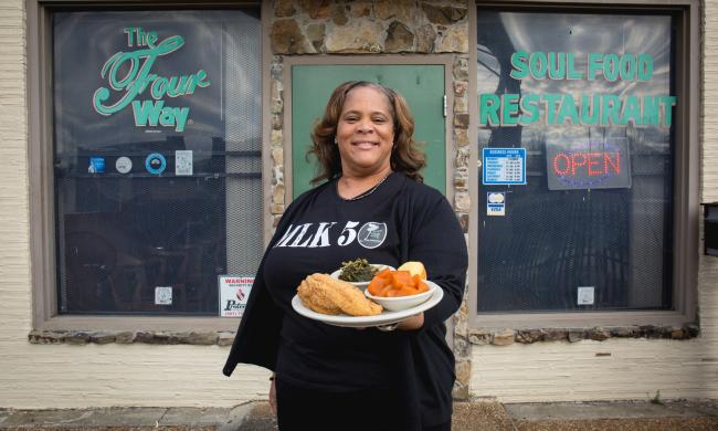 Owner of The Four Way, Patrice Bates Thompson, holding a plate of fried catfish, cornbread and two southern sides outside the restaurant.