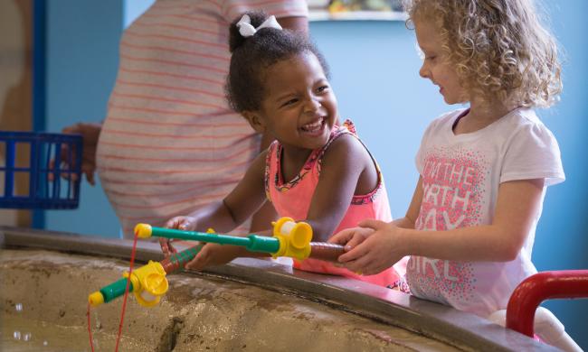 Two girls fishing with plastic toy fishing poles at an exhibit at the Children's Museum of Memphis.