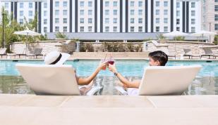 Couple tapping drink glasses together while lounging at the pool at Guesthouse at Graceland.